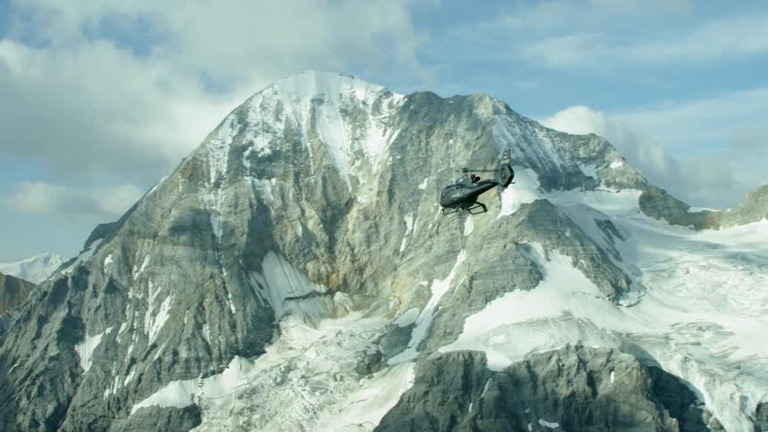 Helicopter flying near snowy mountains on a cloudy day
