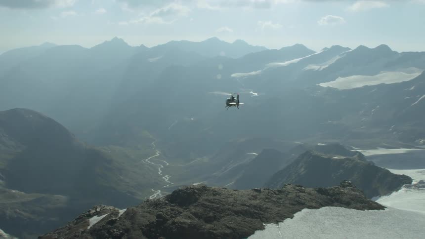 A helicopter is moving past the top of the mountain