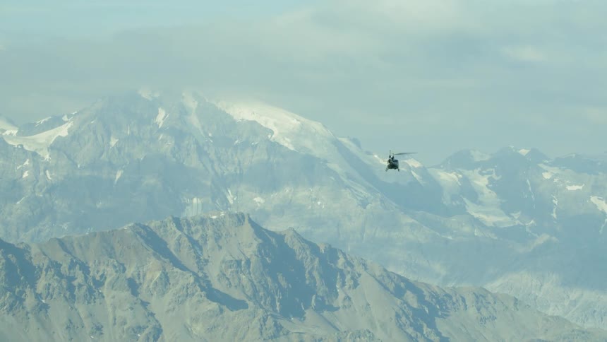A helicopter flies above mountains