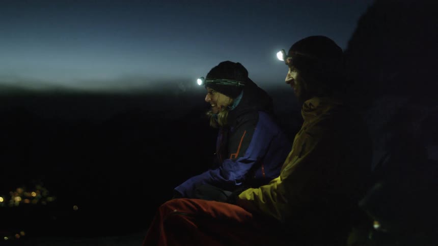 Two men wear head lamps at a campsite at night