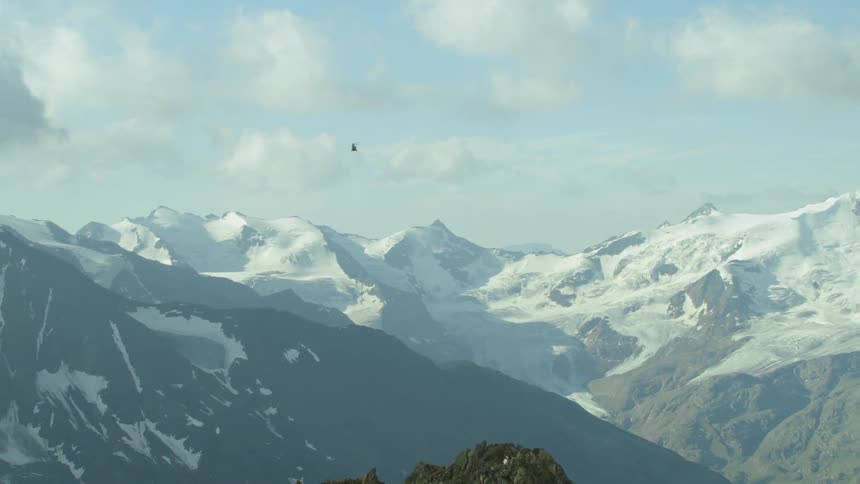 The helicopter moves towards the clouds ahead over the mountains