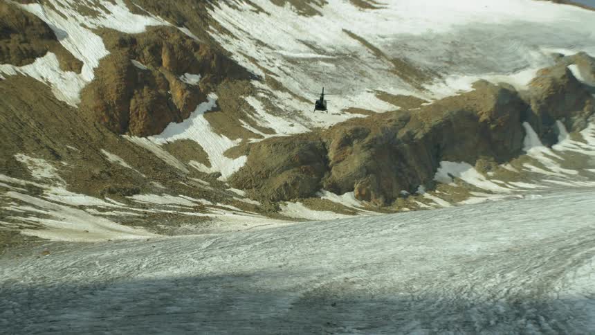 The helicopter is moving up rising over the snow covered mountain