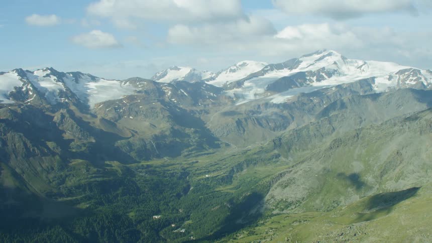 Green valley surrounded by snow-covered mountains on a cloudy day