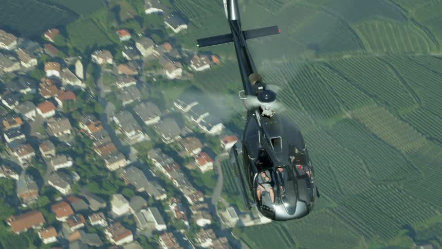 A helicopter flies over crop fields and a neighborhood