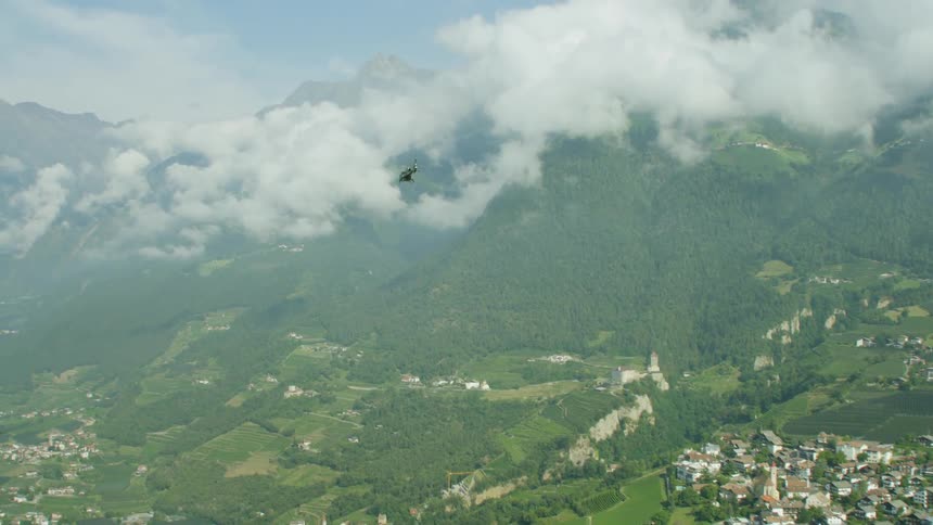 Helicopter flying near mountains and over a small town on a cloudy day