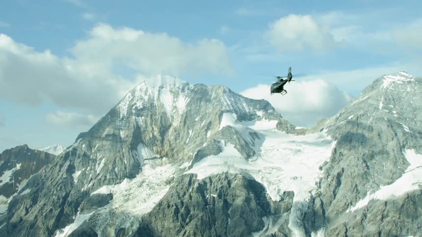 A helicopter flies above the tall snowy mountains