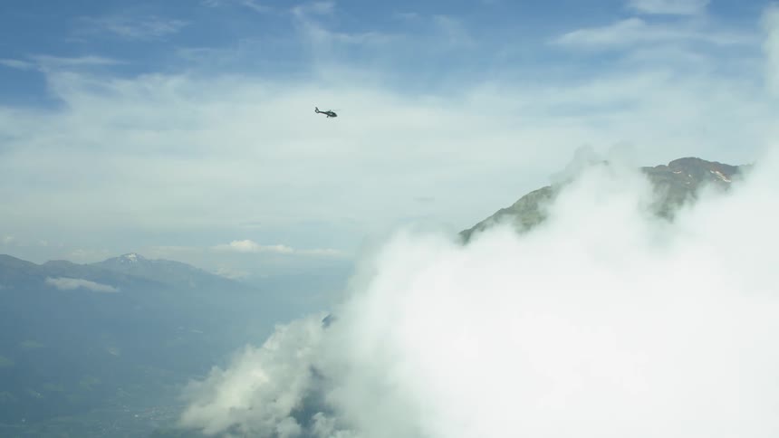 A helicopter flies over clouds and a rocky peak