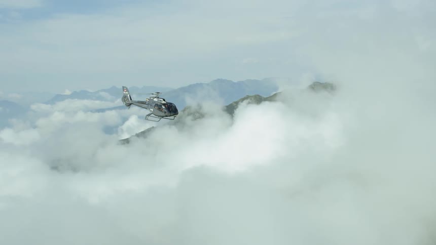 A helicopter is flying above the clouds over a mountain range during the day