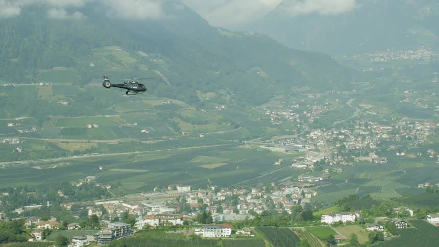 A helicopter is flying above a town in a mountain valley during the day