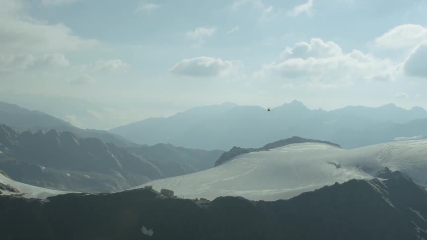 A helicopter is flying above a mountain range in daylight