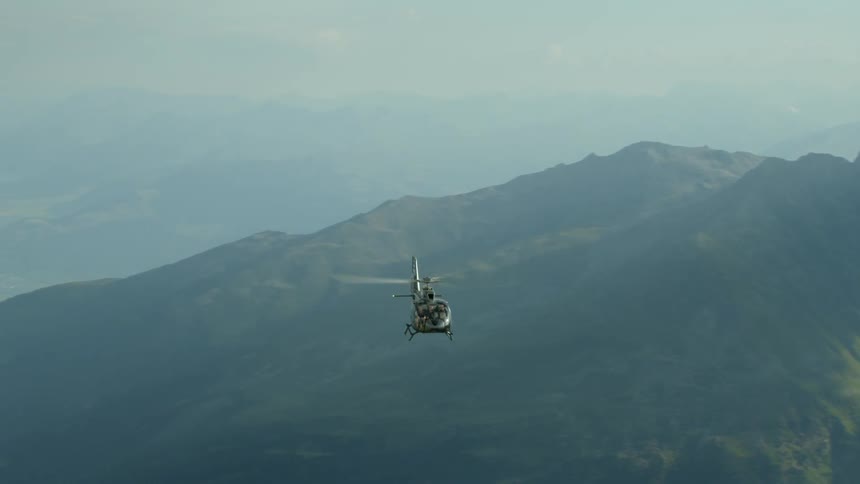 Helicopter flying between mountains on a cloudy day