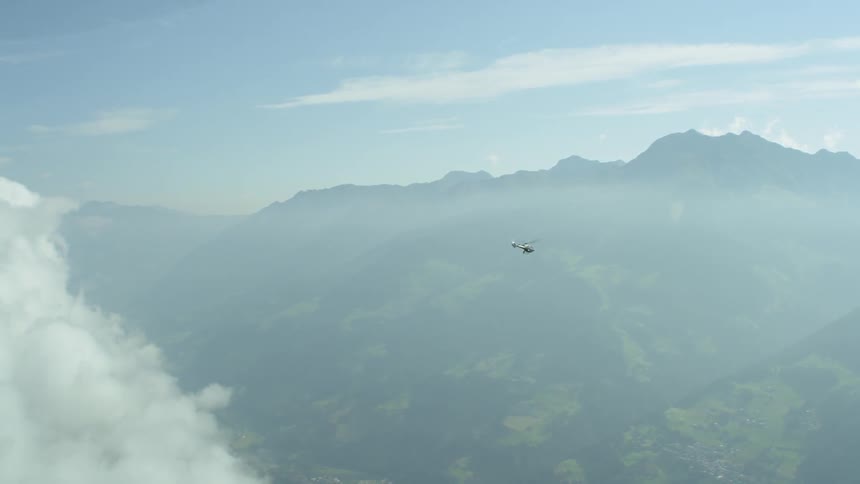 A helicopter is flying above a mountain range in daylight