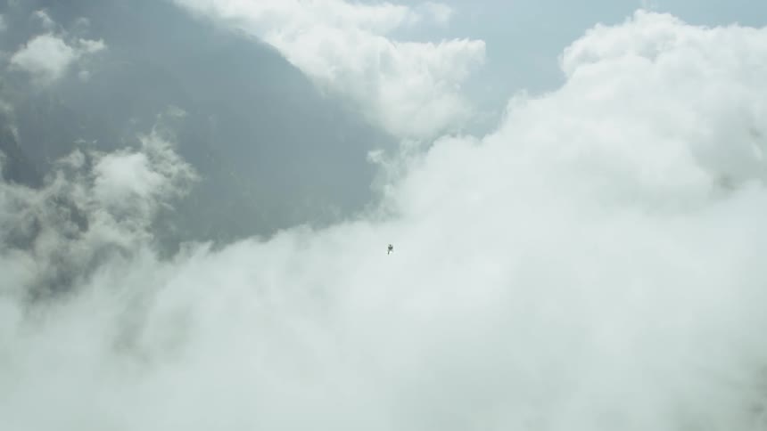 A helicopter flies over clouds in the mountains