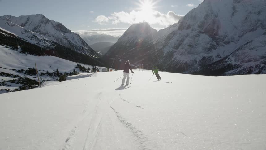 Two skiers are skiing down a mountain slope during the day