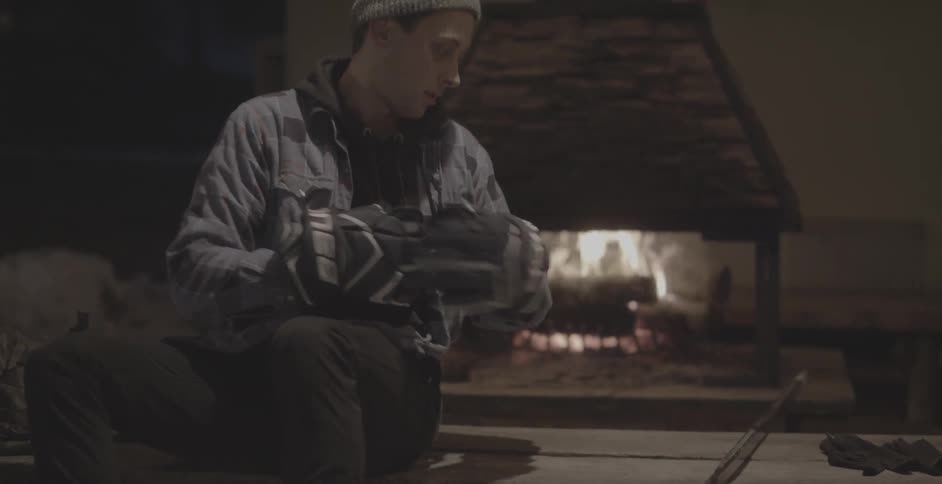A man sits by a fire and puts hockey gloves on