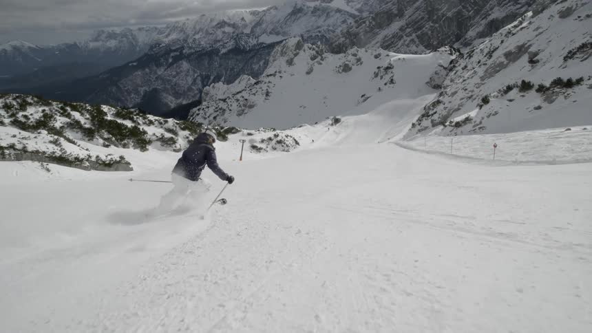 A woman skiing in snowy mountains with fluffy white clouds in the sky