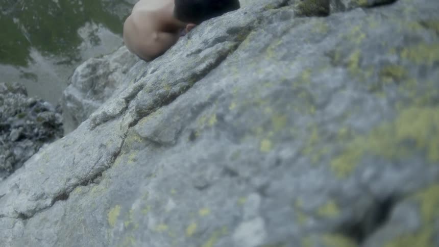 A man is lying naked on a mountain ledge during the day