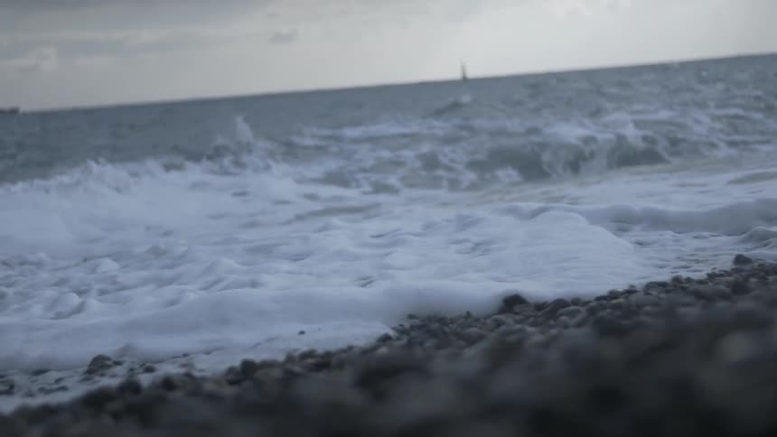 An ocean wave is crashing onto a beach on a cloudy day
