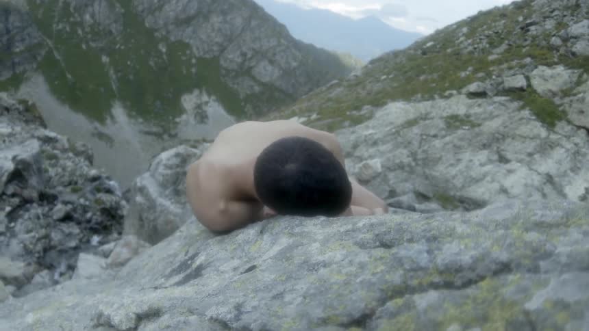 A man is lying naked on a mountain ledge during the day