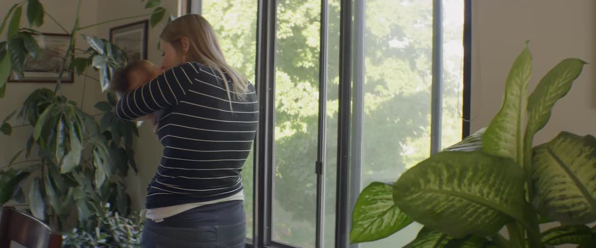 A woman rocks a newborn next to a window
