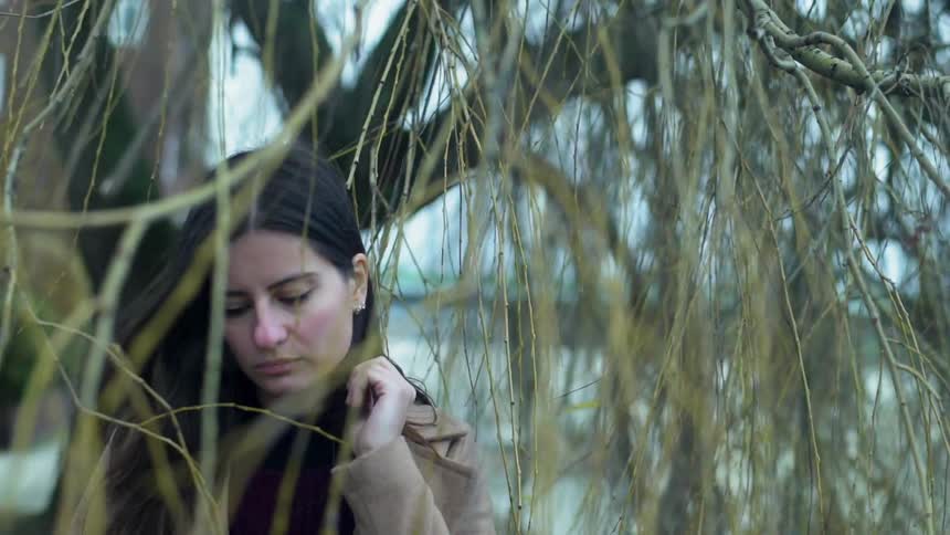 Woman standing under a tree and brushing some hair behind her left ear