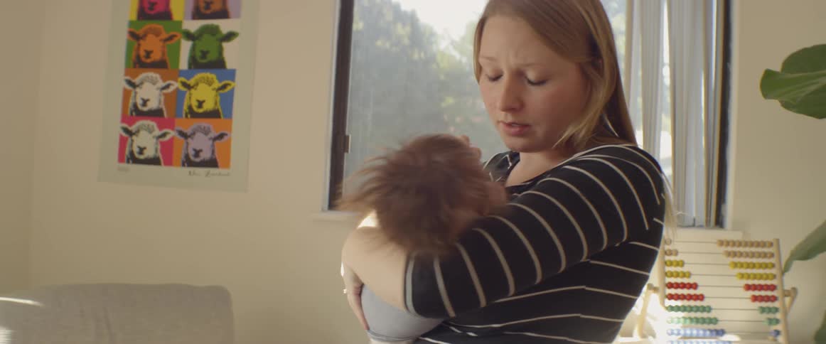 A woman is holding and rocking a baby in her arms inside in daylight