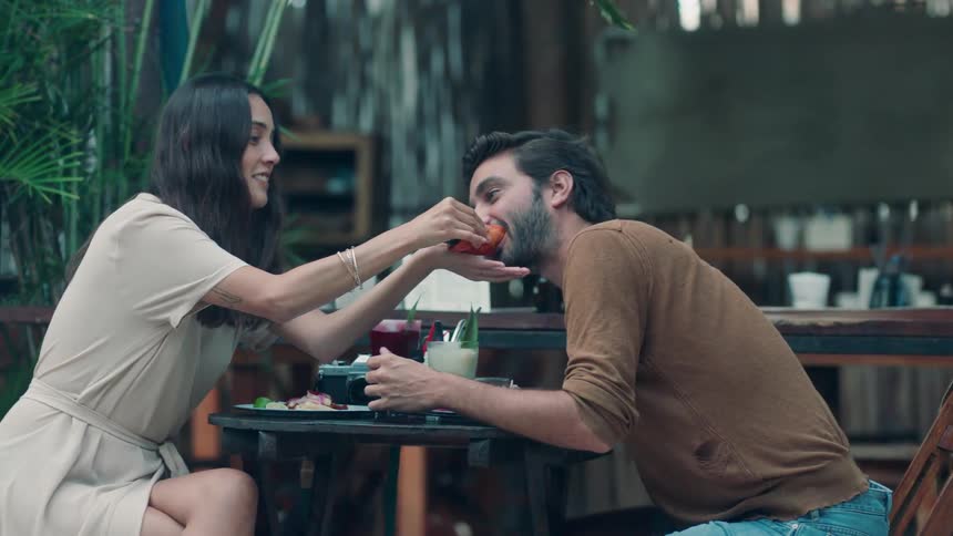 A woman gives a man a taste of her food at an outdoor table