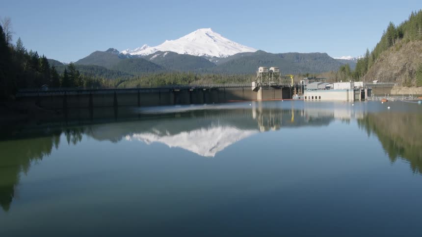 Revealing the reflection of a snow covered mountain in the mirror calm water of a hydroelectric dam reservoir