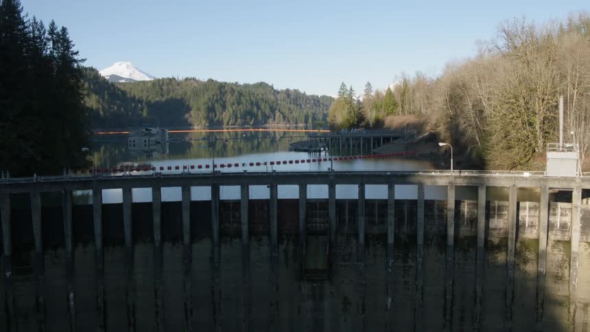 Ascending straight up the face of a tall concrete dam to reveal the deep reservoir behind it