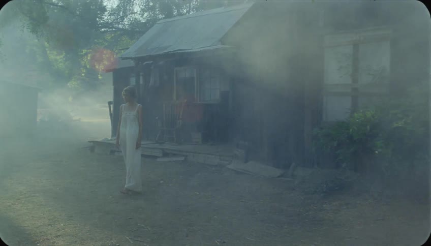 A woman walks out of a cabin in her nightgown as wind blows smoke past