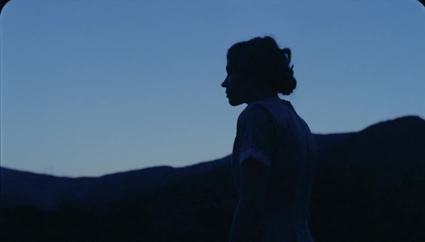 Silhouette of a woman walking by hilly landscape at sunset