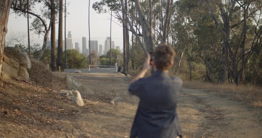 A man takes a photograph of skyscrapers in the distance