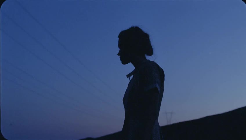 Woman standing outdoors as several power lines line the clear sky near dusk