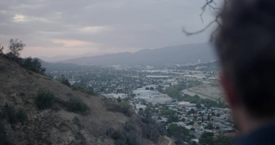 Man stands on a hilltop overlooking a city