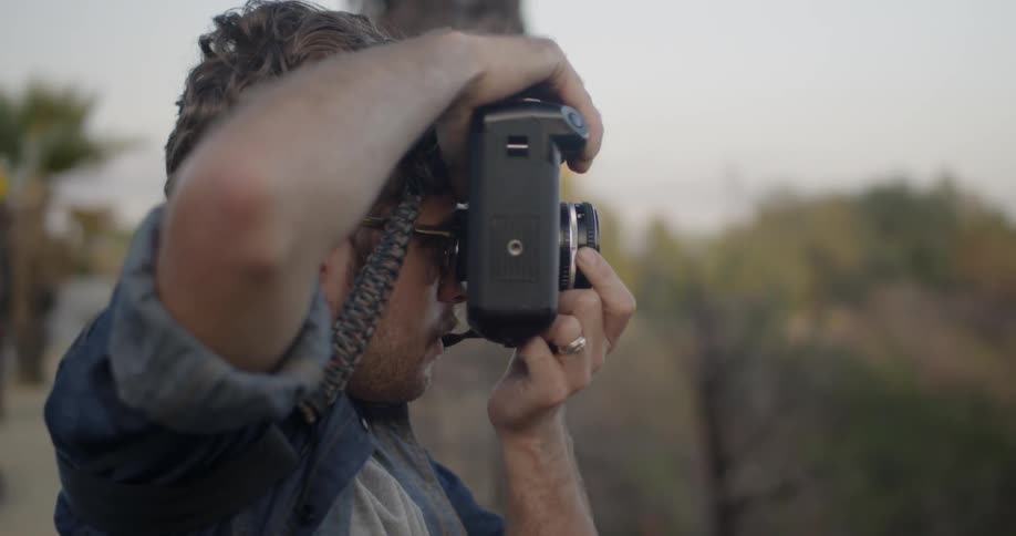A man focuses his camera lens while taking a photo outside