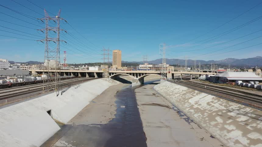 Cars travel across a bridge over train tracks and dried up river