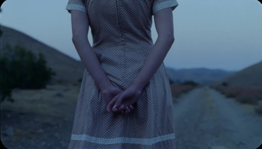 A woman walks down a dirt road with her hands clasped behind her back