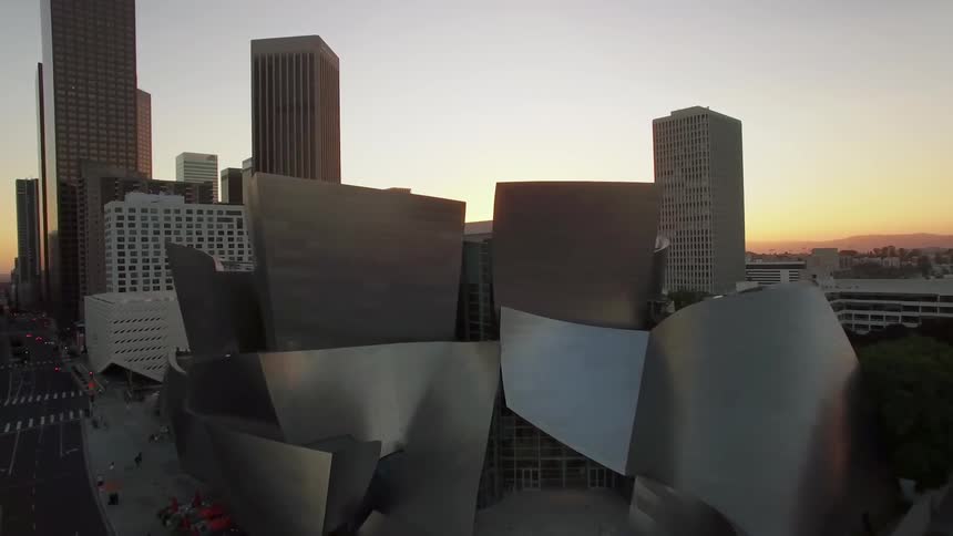 The sun is rising beyond an architecturally interesting building in a city