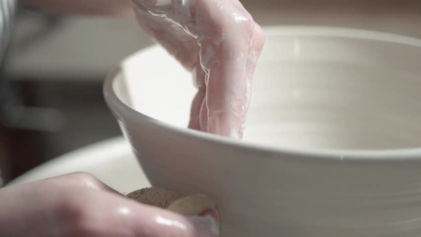 A woman is forming a bowl on a pottery wheel during the day