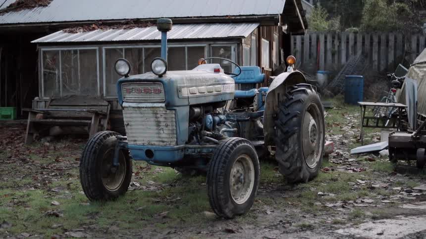 Blue tractor outside of a dilapidated house
