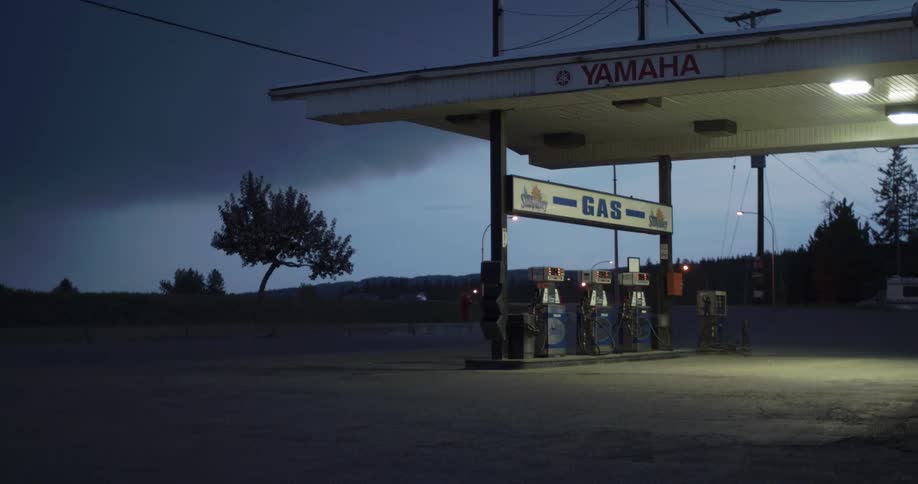 Traffic passes by on a road near a gas station at dusk