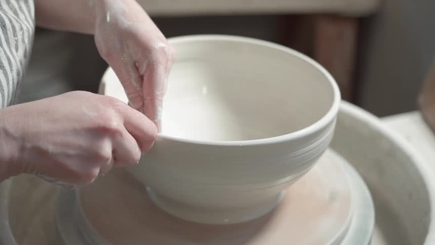 A woman is forming a bowl on a pottery wheel during the day
