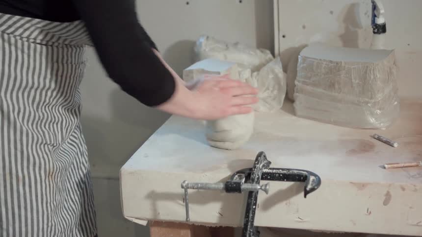 A woman is kneading clay in a workshop during the day