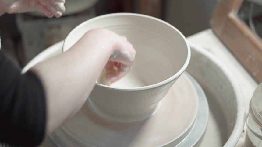 A person is nearly down creating a pot on the clay wheel