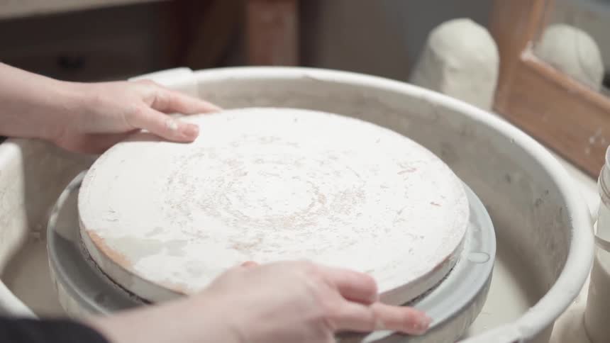 A woman taps down a base on a potter's wheel
