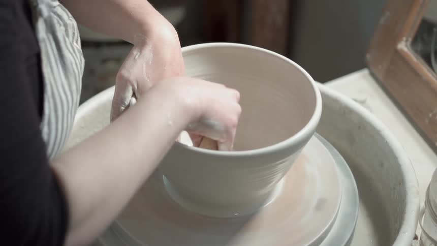 Person wets their hands and forms a bowl on a pottery wheel