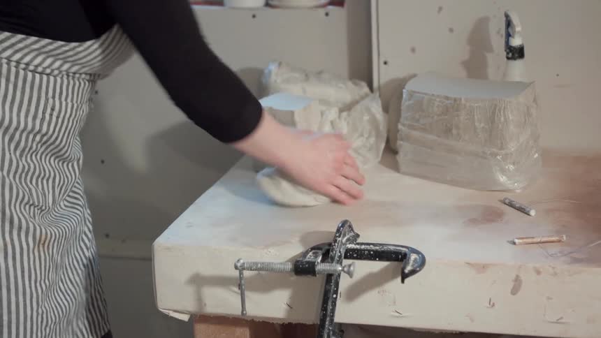 A woman wearing an apron is rolling clay on a counter