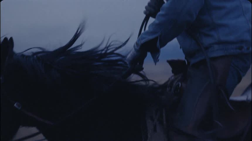 A cowboy rides a horse across a rural field
