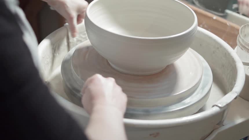 A woman is trimming a piece of pottery she is forming on a wheel