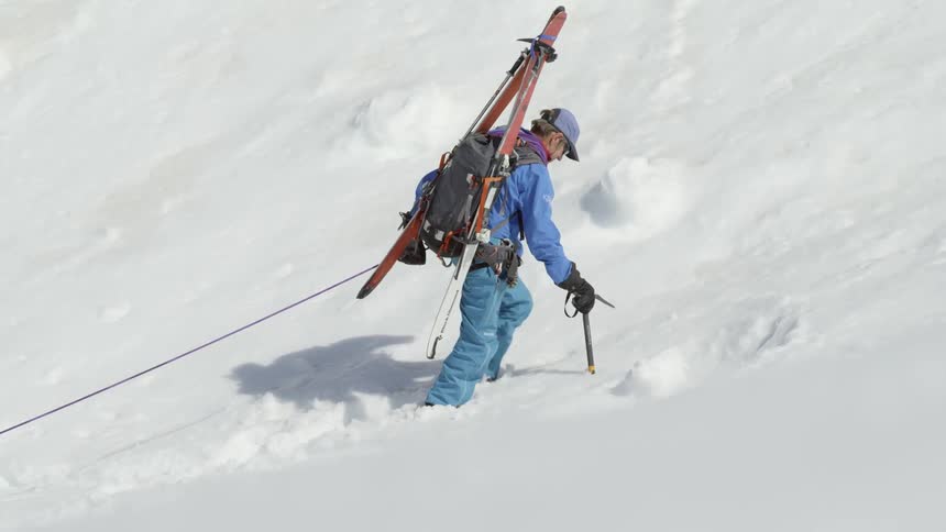 A man with skis on his back climbs up a mountain slope